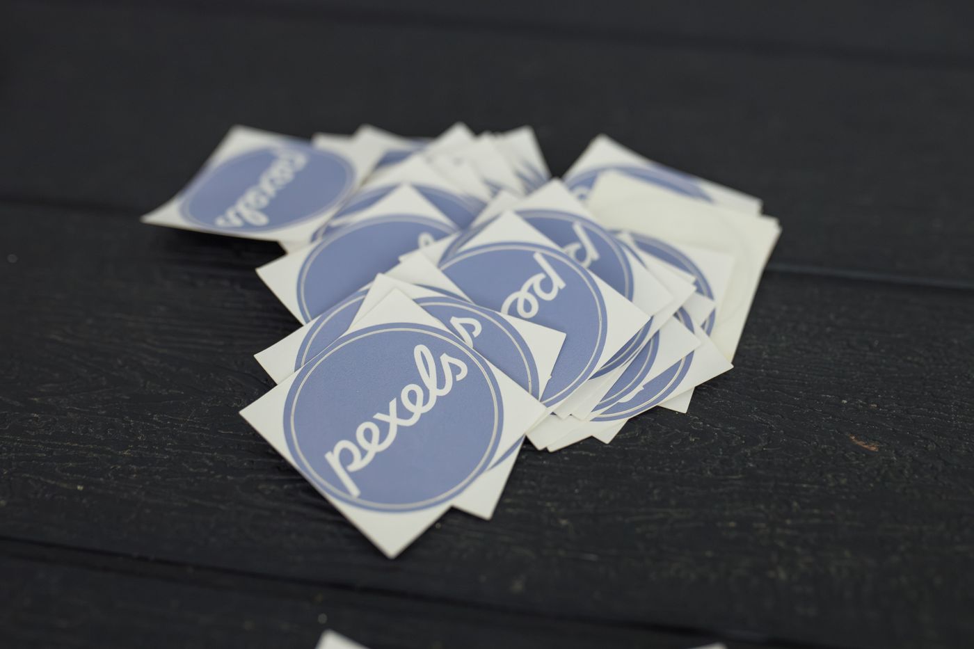 custom stickers in any shape — A pile of Pexels logo stickers arranged on a dark wooden surface