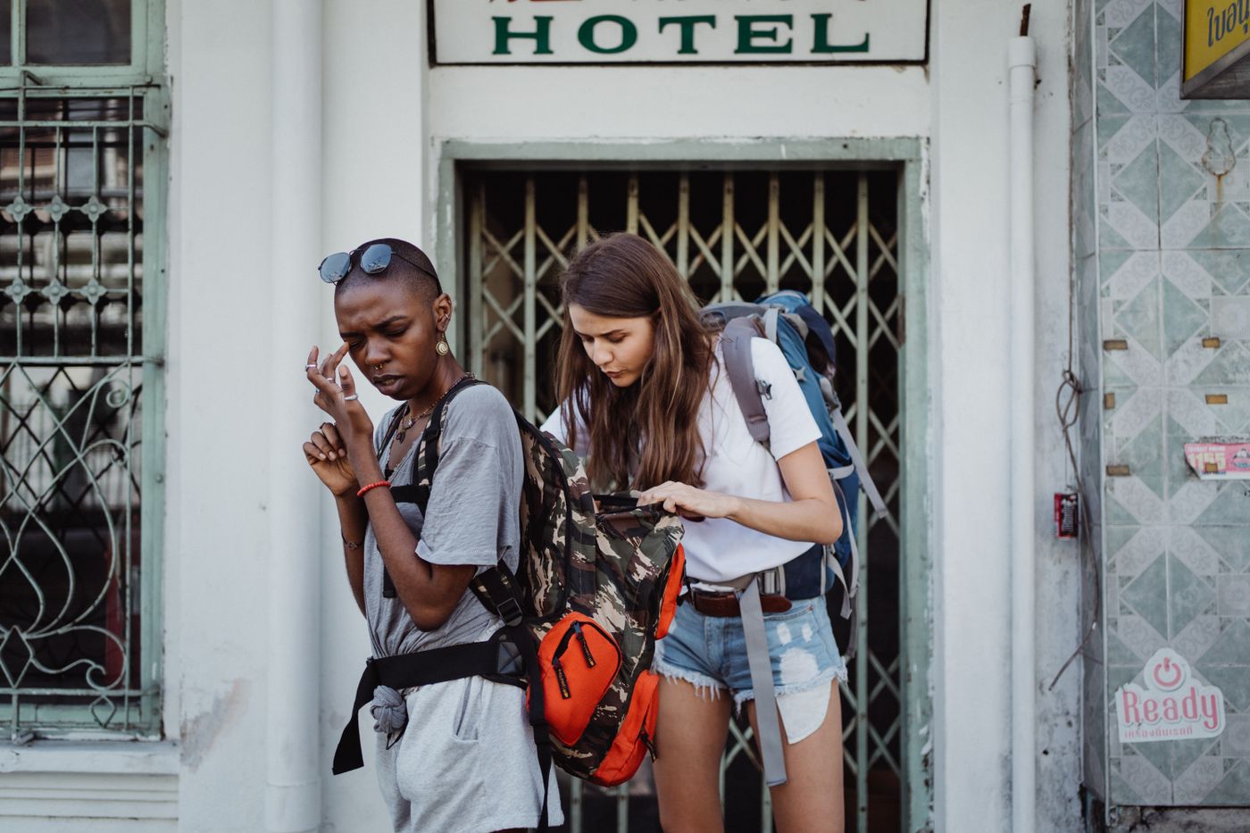 name tag keychain for backpack — Two young female backpackers checking their belongings outside a hotel entrance