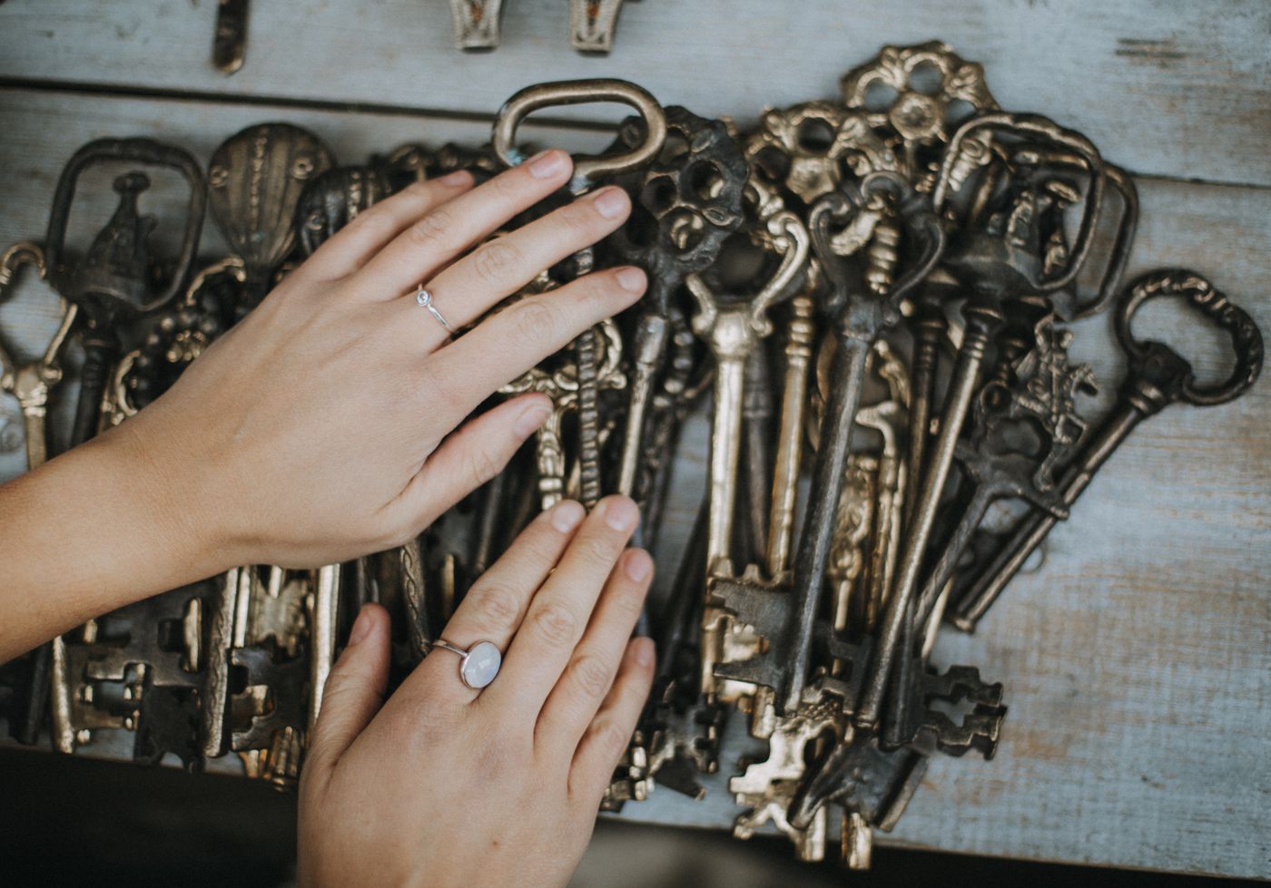 3d printed keychain custom name — Close-up view of hands with rings holding an array of vintage skeleton keys on a wooden surface