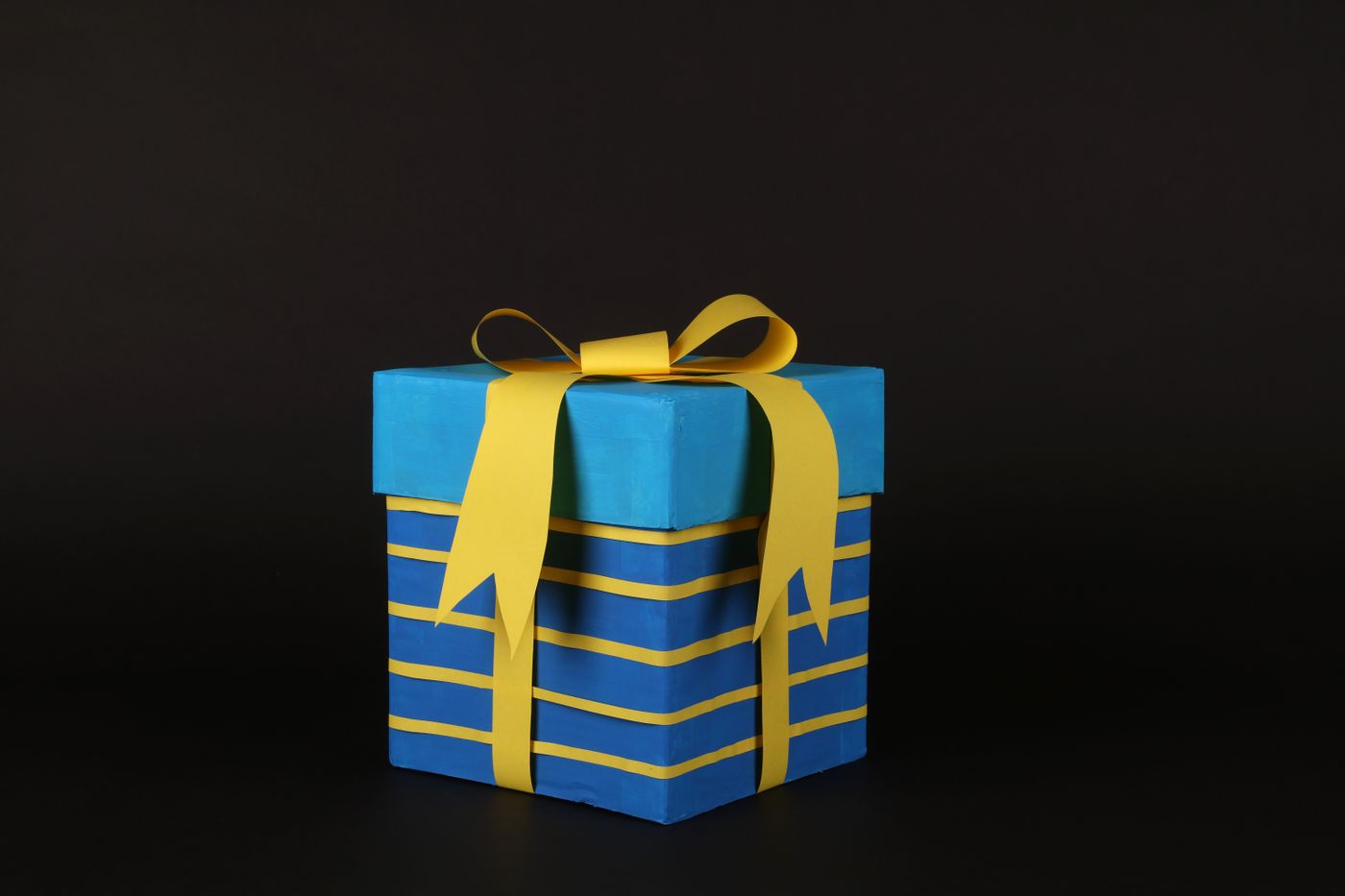 3d printed marriage gift — Vibrant blue gift box wrapped in yellow ribbon on black background for celebrations