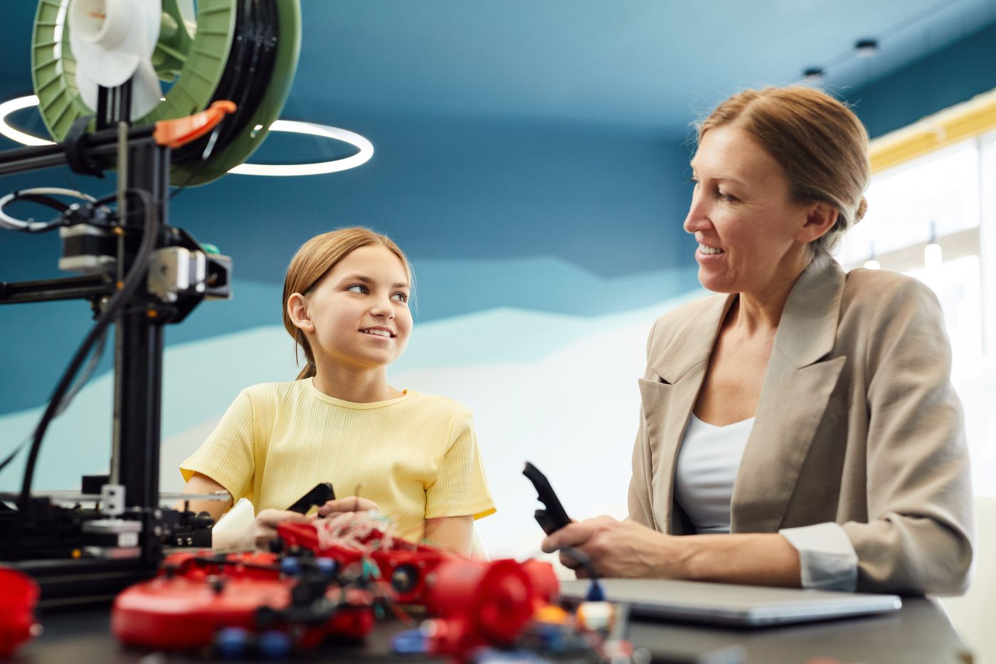 3d printed gift for 8 year old girl — Low angle of smiling woman and little girl sitting at table and working on engineering project together while looking at e