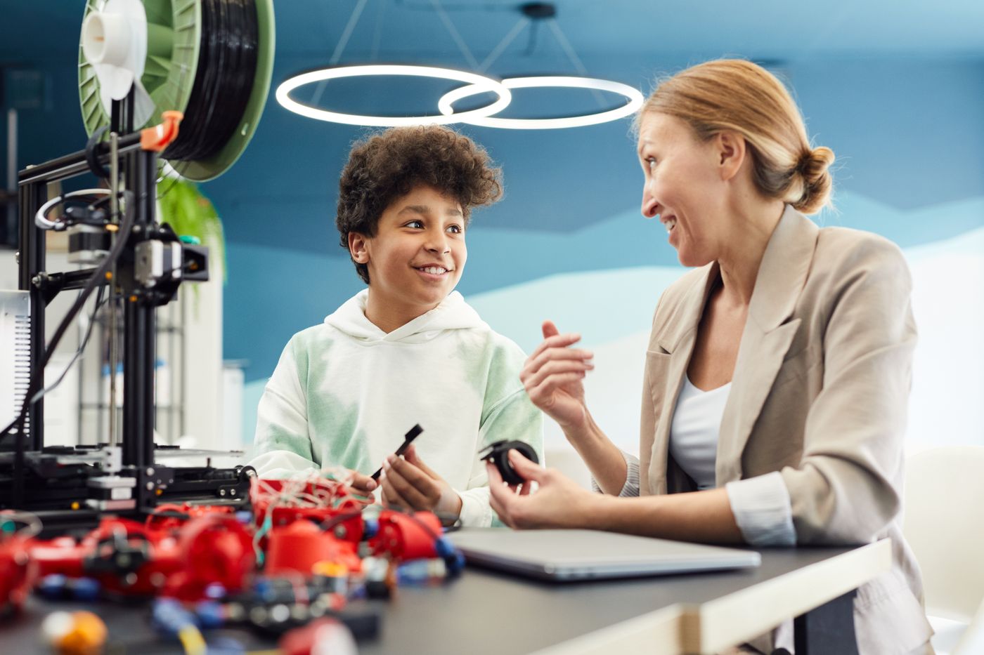3d printed gift for 8 year old girl — Smiling young male engineer sitting at table with woman and discuss project together while looking at each other in light 