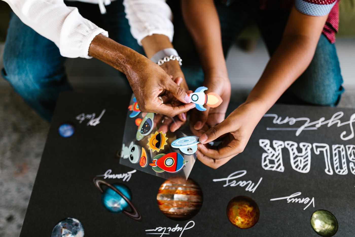 custom shape kiss cut stickers — Two people collaborating on a solar system art project with stickers