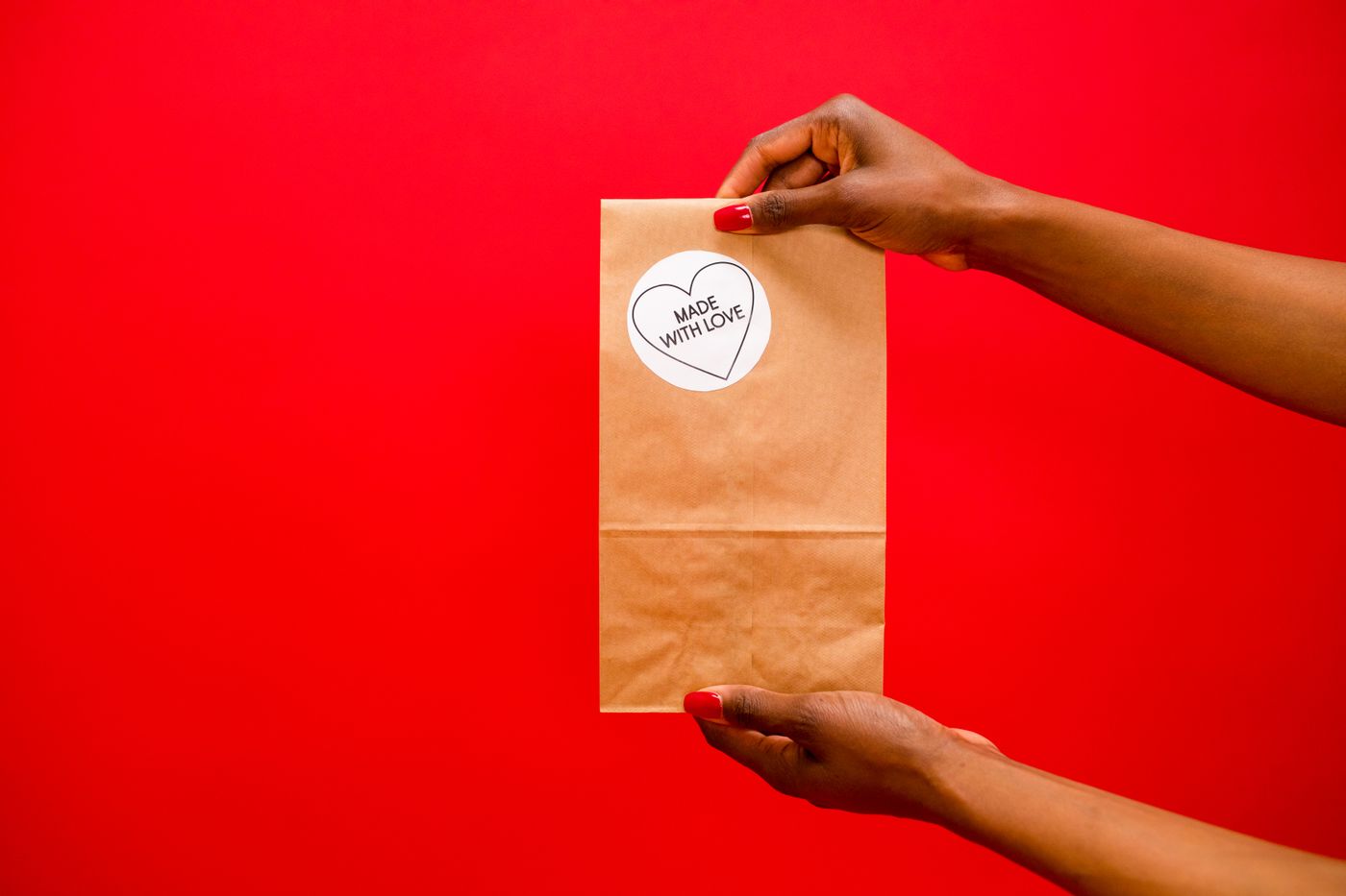 cartoon stickers for wall — Brown paper bag with 'Made With Love' label held by hands over a red background