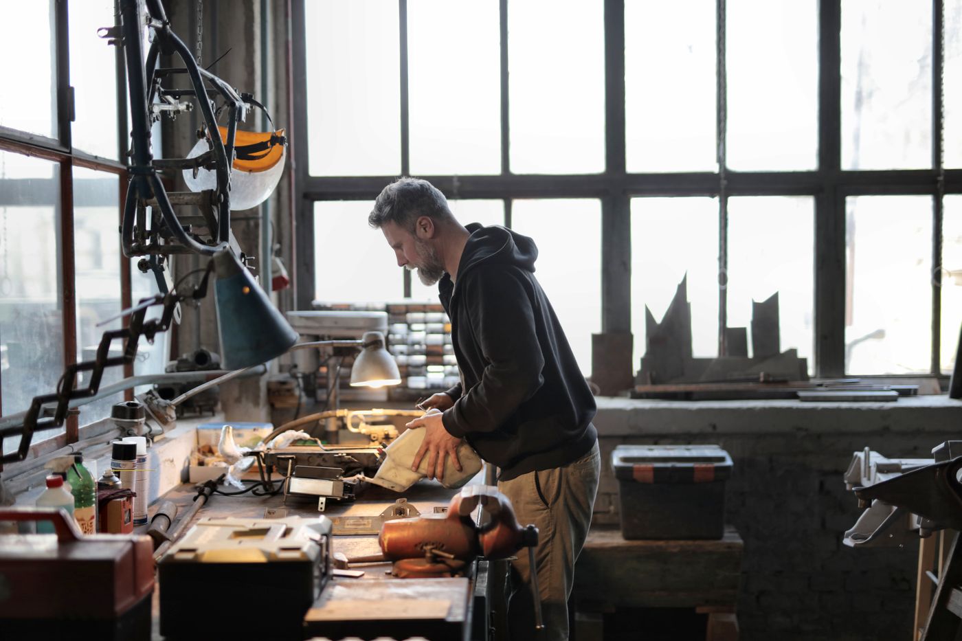 3d print for keychain — Side view of male workshop owner standing near messy workbench and fixing metal details while using instruments during work