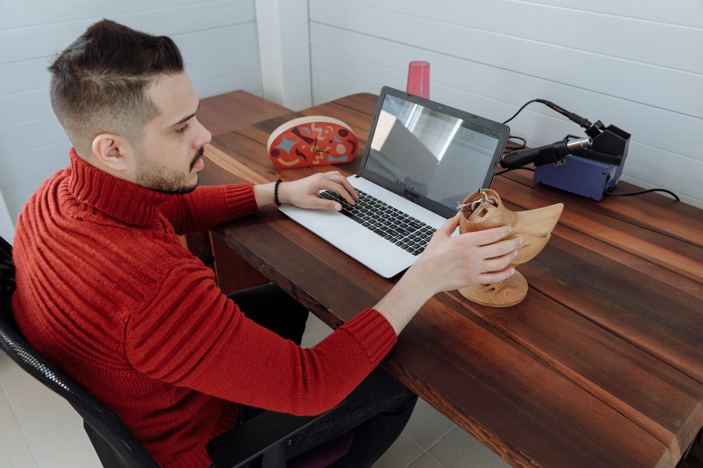 3d printed gift for girlfriend — Engineer working on a laptop at a wooden desk, holding a 3D model in an office setting