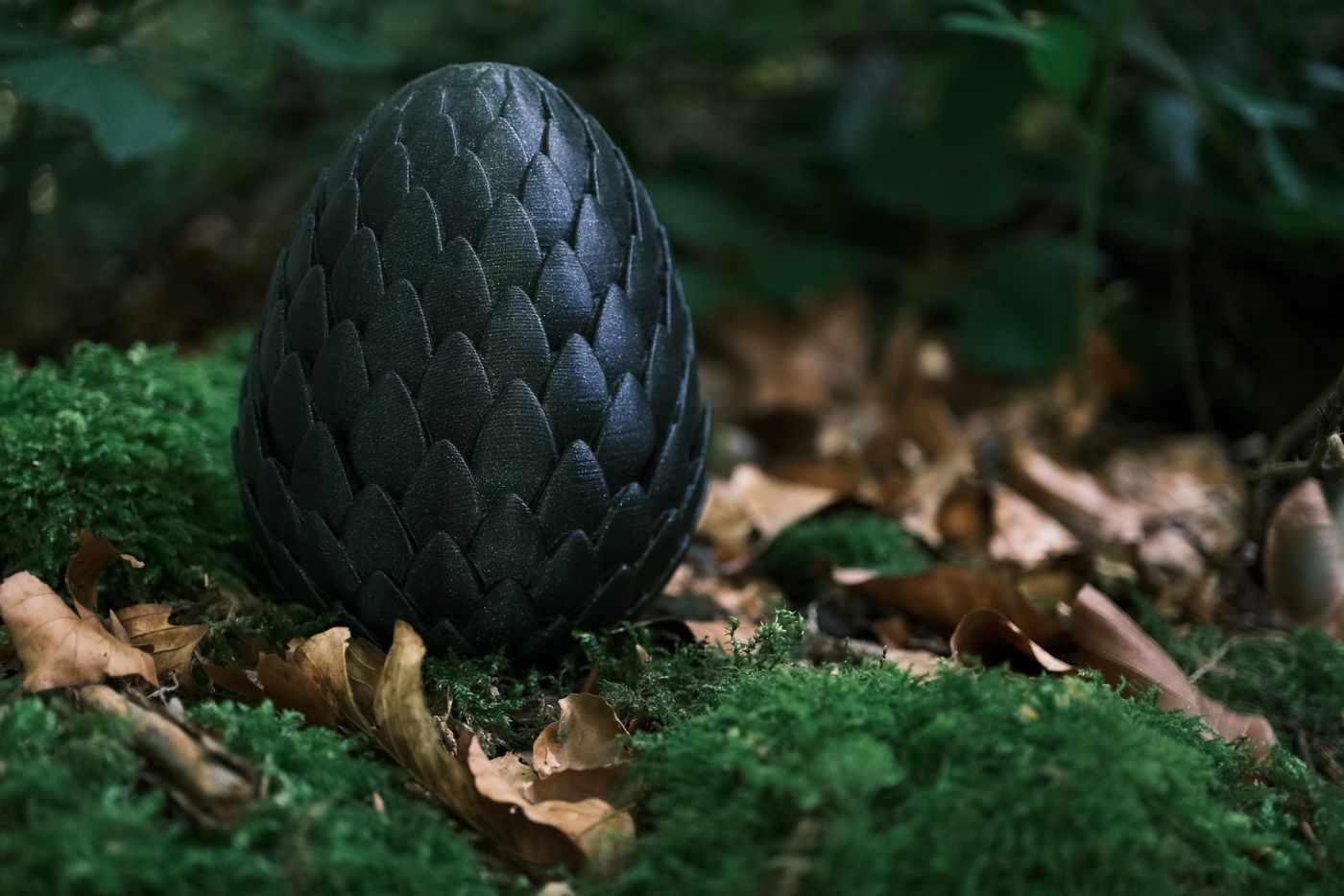 3d printed gift for girlfriend — Intriguing black dragon egg-like sculpture set in a lush forest environment, surrounded by moss and leaves