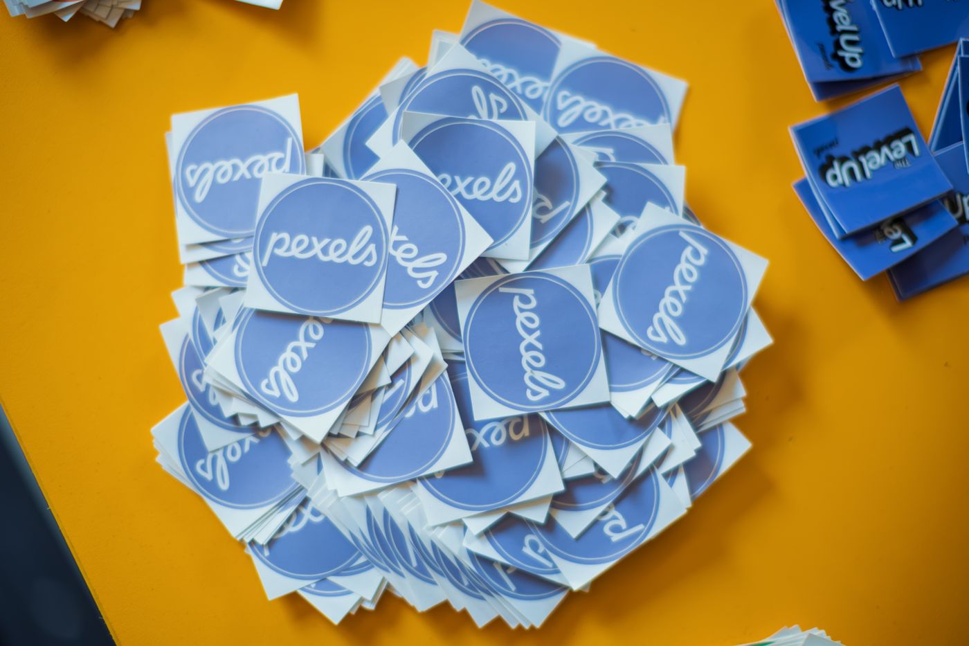 how to print custom shape stickers — Pile of blue Pexels stickers on a vibrant yellow surface, top view