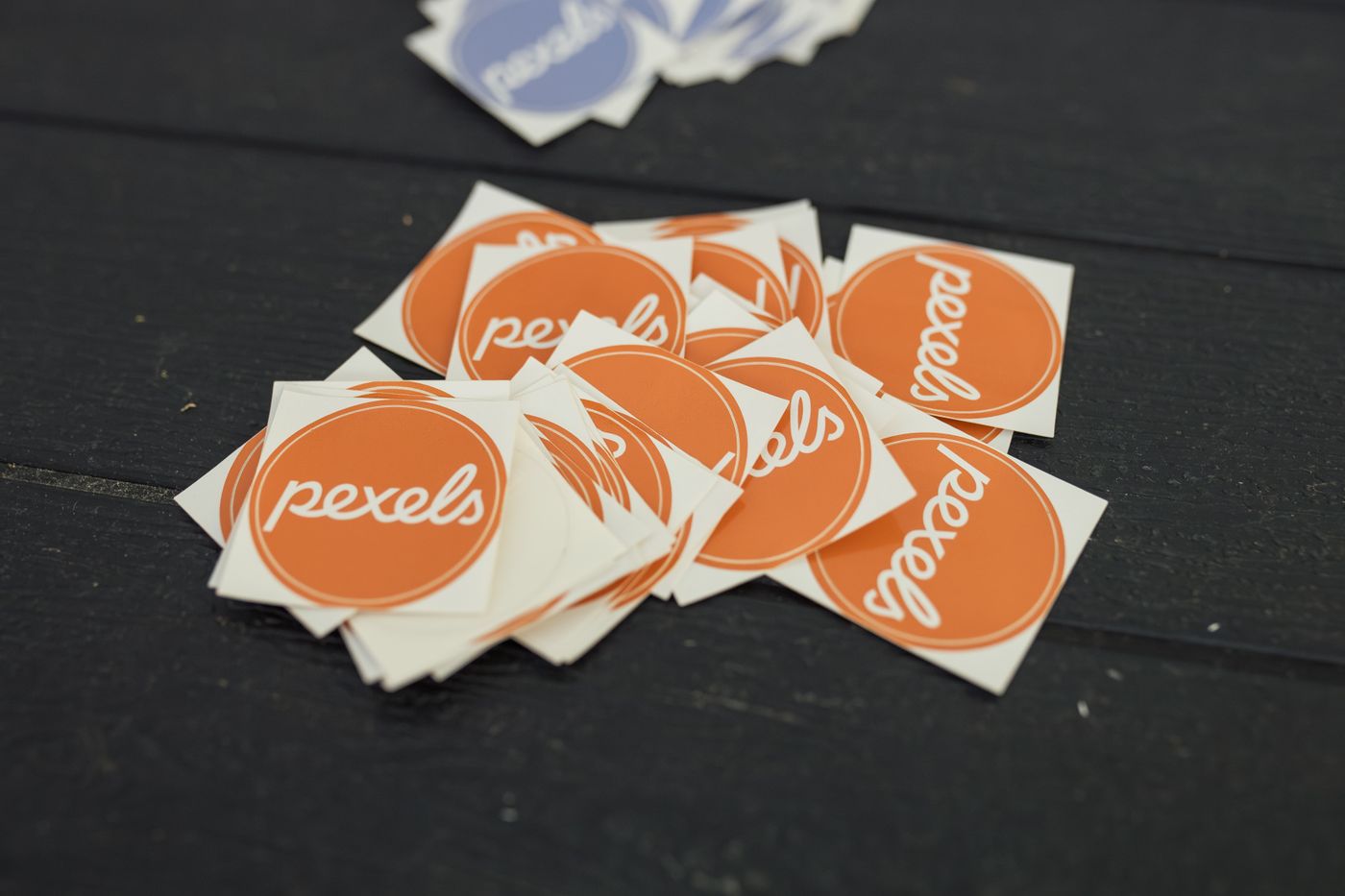 how to print custom shape stickers — A pile of Pexels logo stickers in orange and blue on a dark wooden table