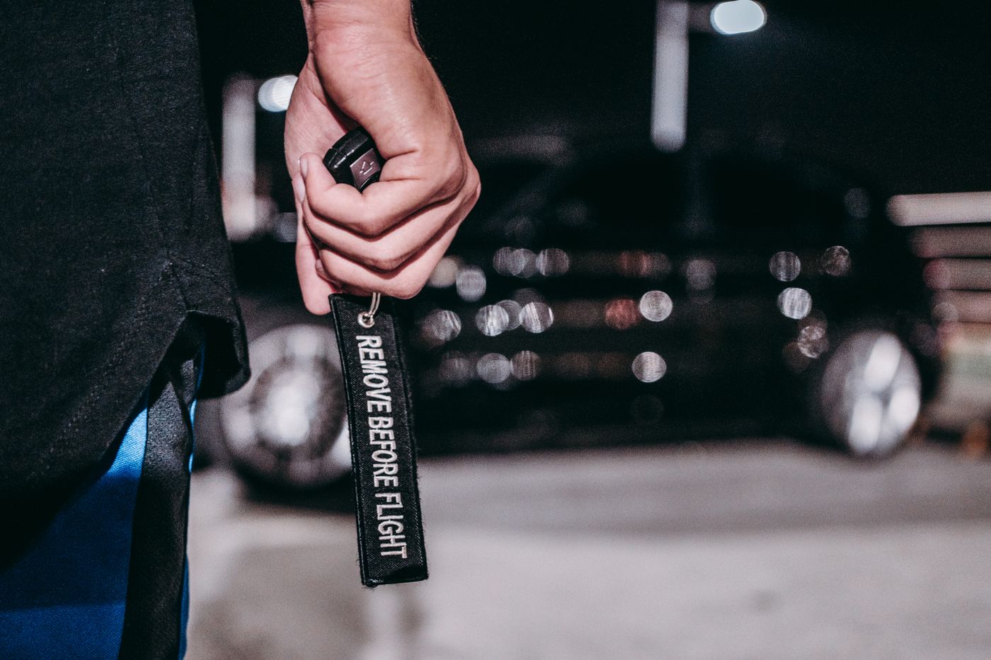 name keychain maker online — A hand holding a 'Remove Before Flight' keyring in front of a blurred car at night