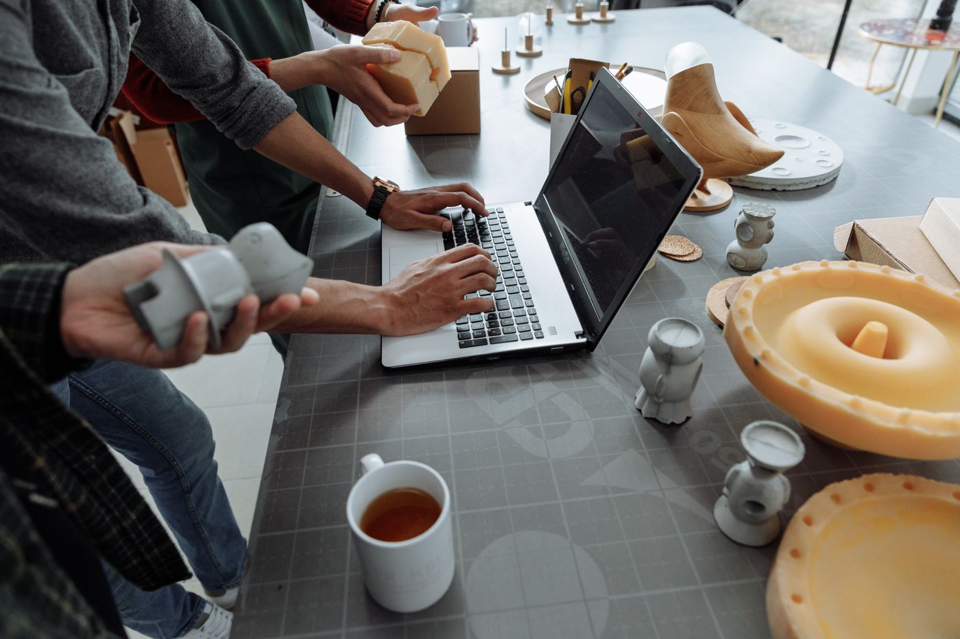 3d print design tips — Hands on laptop in a creative workspace with 3D models and prototypes