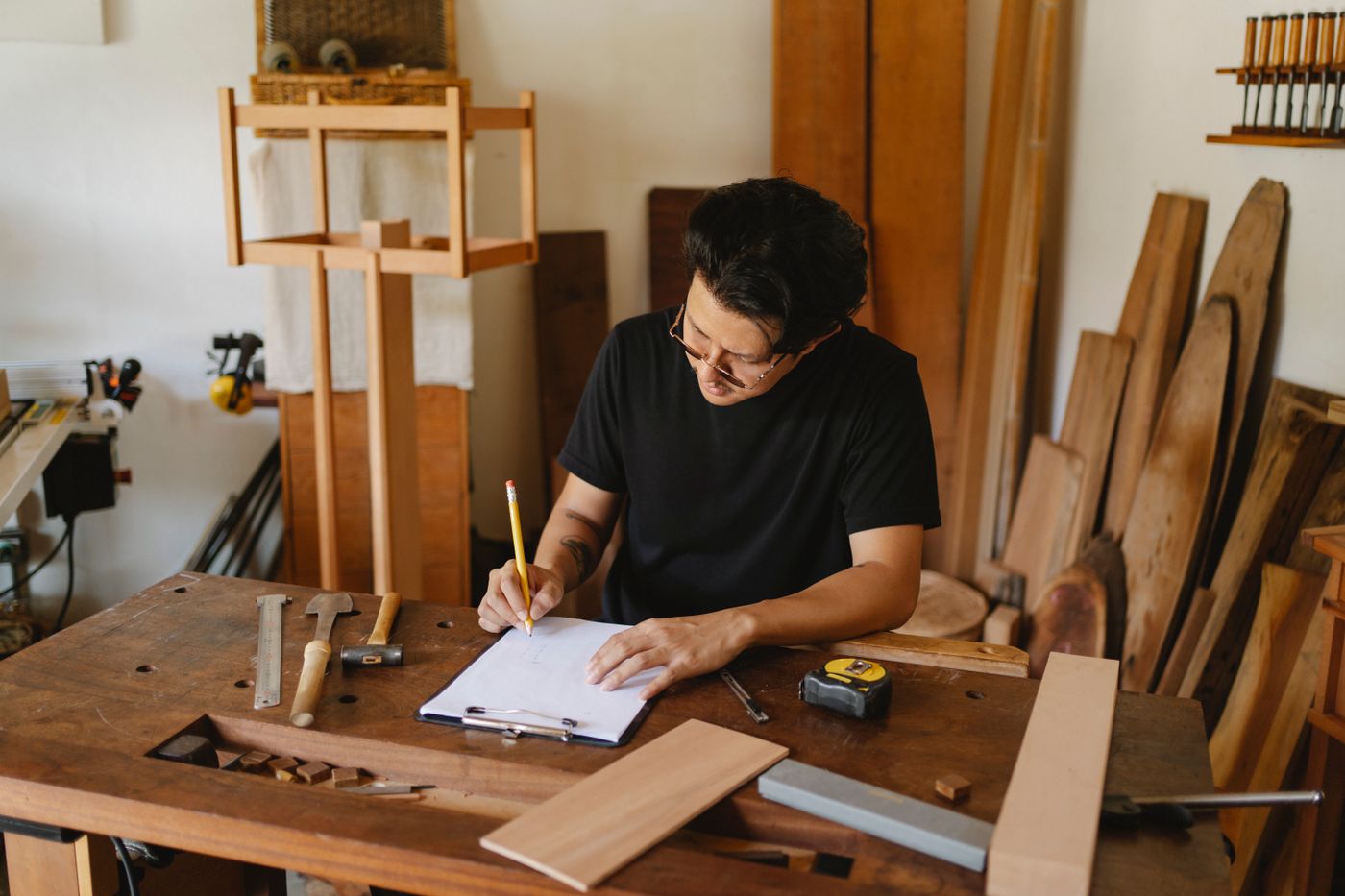 3d printer keychain price — Concentrated man in glasses sitting at wooden table in workshop and holding pencil while creating new object on paper