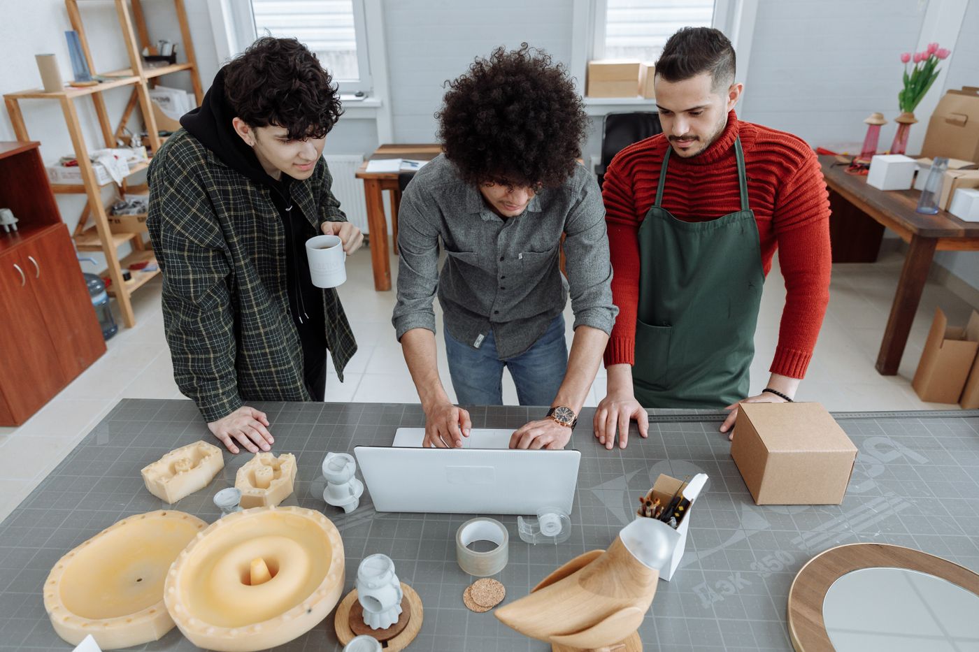 3d printer keychain price — Three men in a workshop setting working together with a laptop and various crafting materials on the table