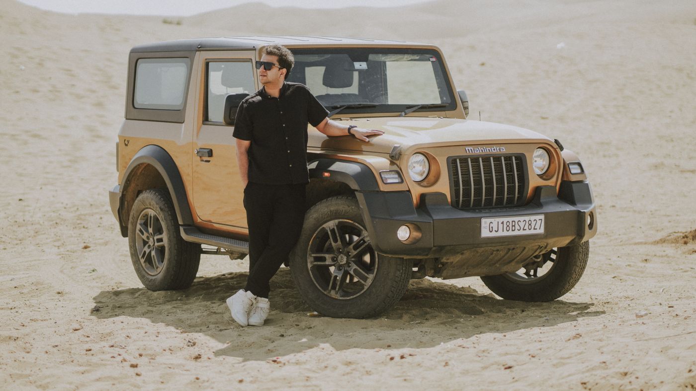 thar keychain — A stylish man in sunglasses leans on a Mahindra Thar SUV amidst a vast desert setting