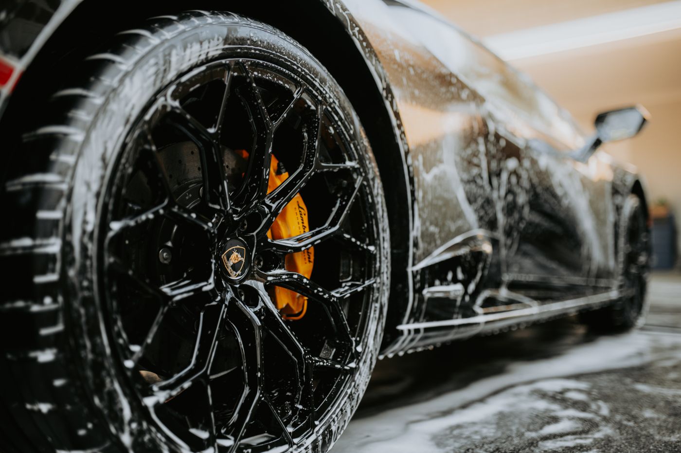 ev car keychain india — Detailed close-up of a luxury car wheel covered in soap suds during a professional car wash
