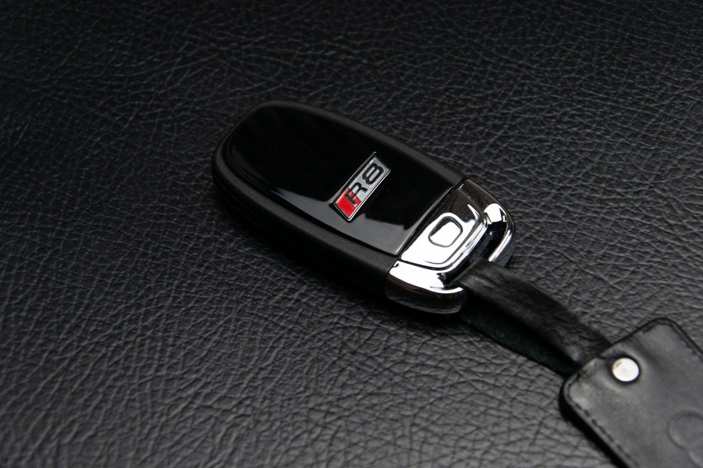 ev car keychain india — Close-up of a luxury car key fob resting on a textured leather surface, symbolizing elegance