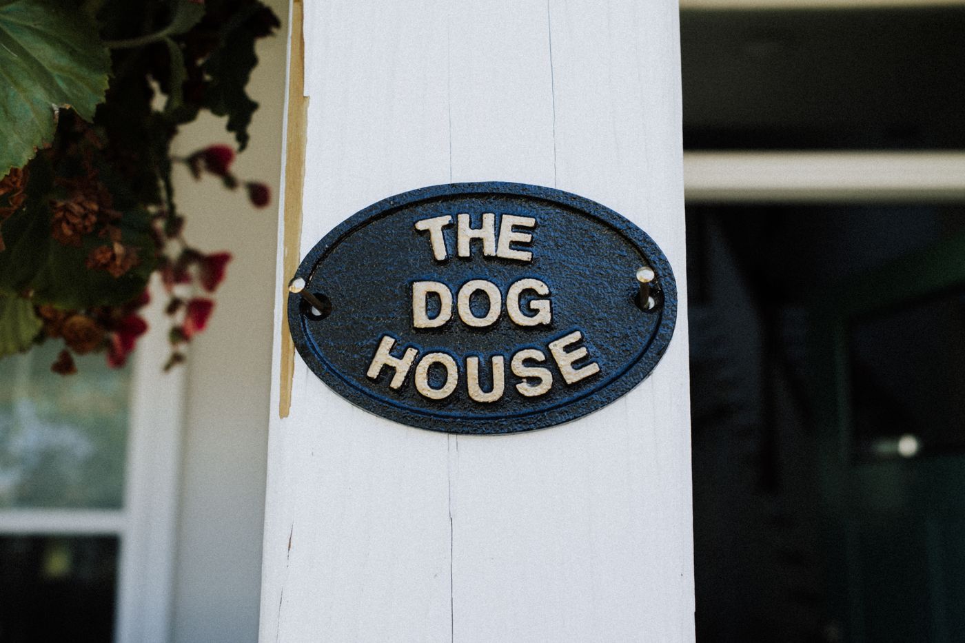 house name plate 3d printed — Close-up of a rustic 'The Dog House' sign on a white wooden post with foliage