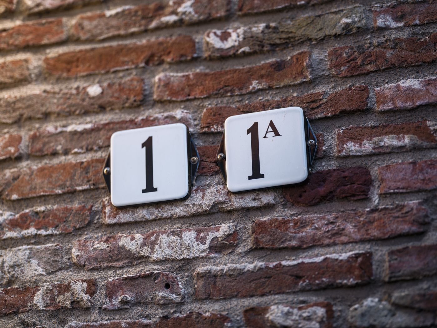 house name plate 3d printed — Close-up of a textured brick wall with mounted street numbers 1 and 1A in focus