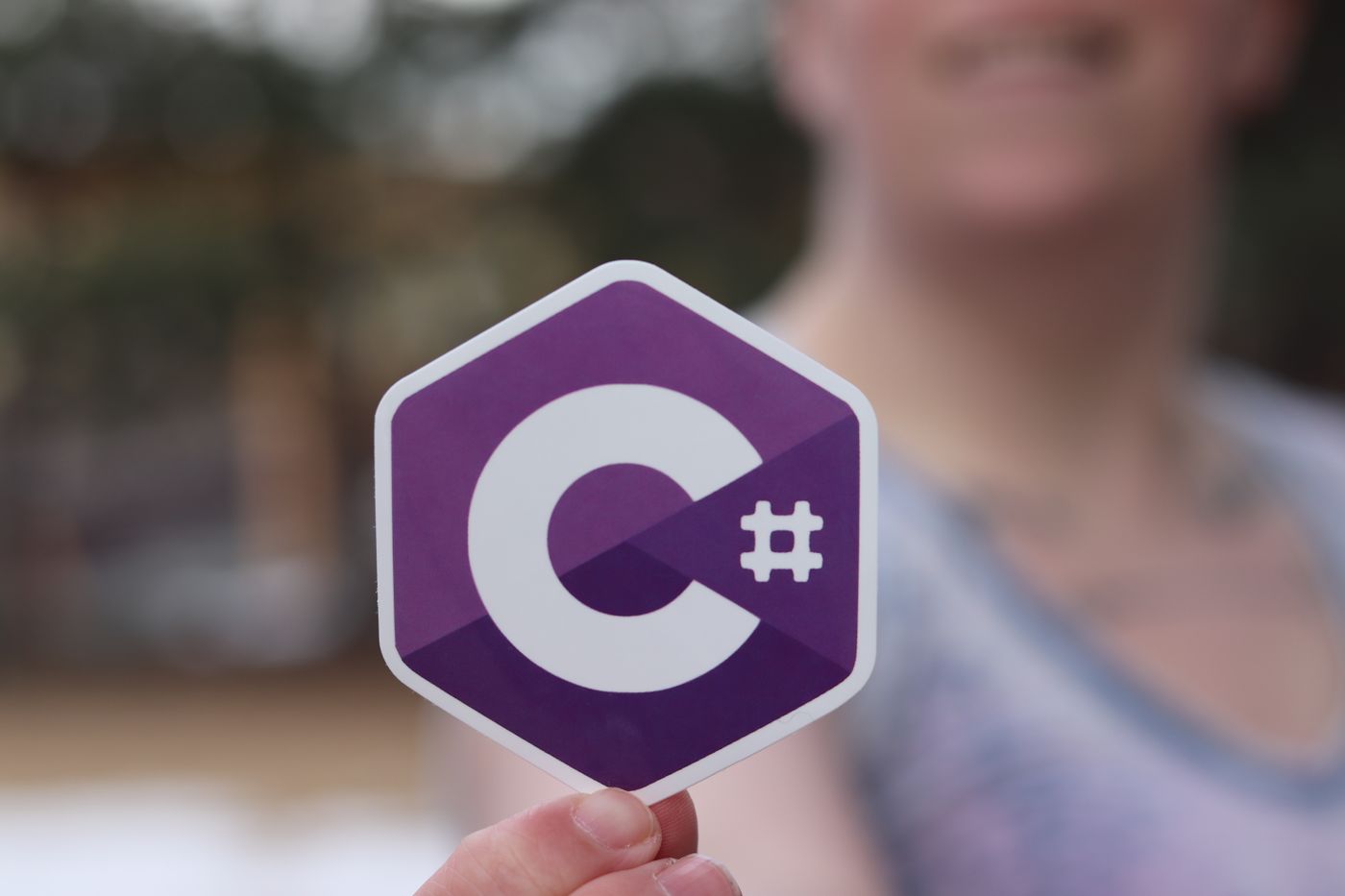 custom sticker sheets — Person holding a C# programming language logo sticker outdoors