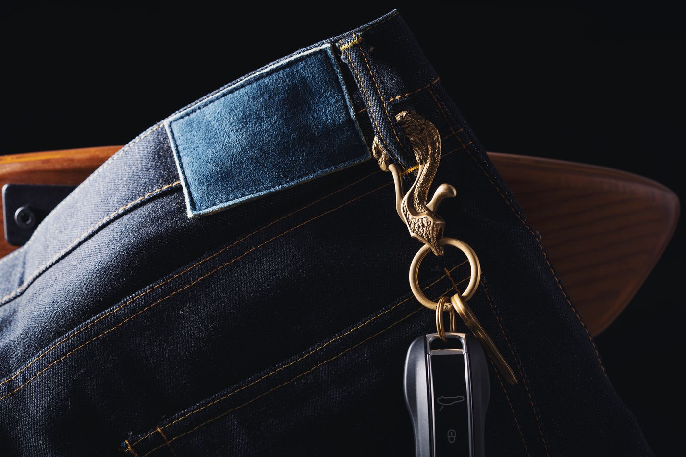 anime keychain — Close-up of denim jeans with a keychain featuring a carved eagle and car key. Stylish accessory detail