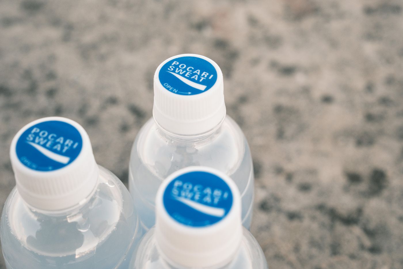 sticker for water bottle — Three Pocari Sweat bottles on a stone surface, focus on blue caps