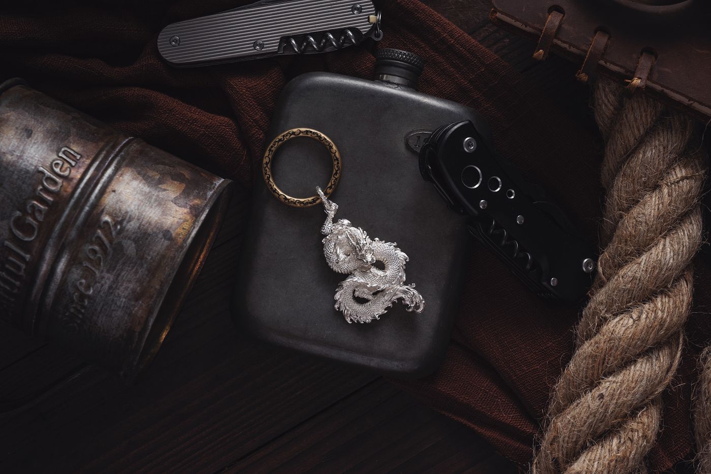 gaming keychain — A flat lay of a dragon keychain, pocket knife, and flask. Perfect for adventure or lifestyle themes