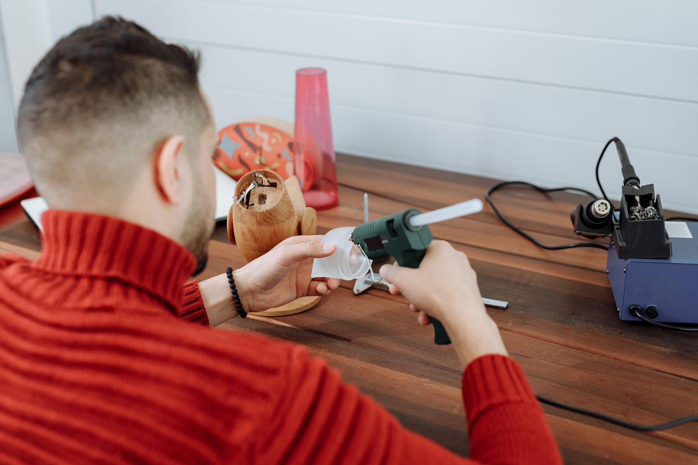 petg print settings — A man in a red sweater using a hot glue gun at a wooden workspace indoors