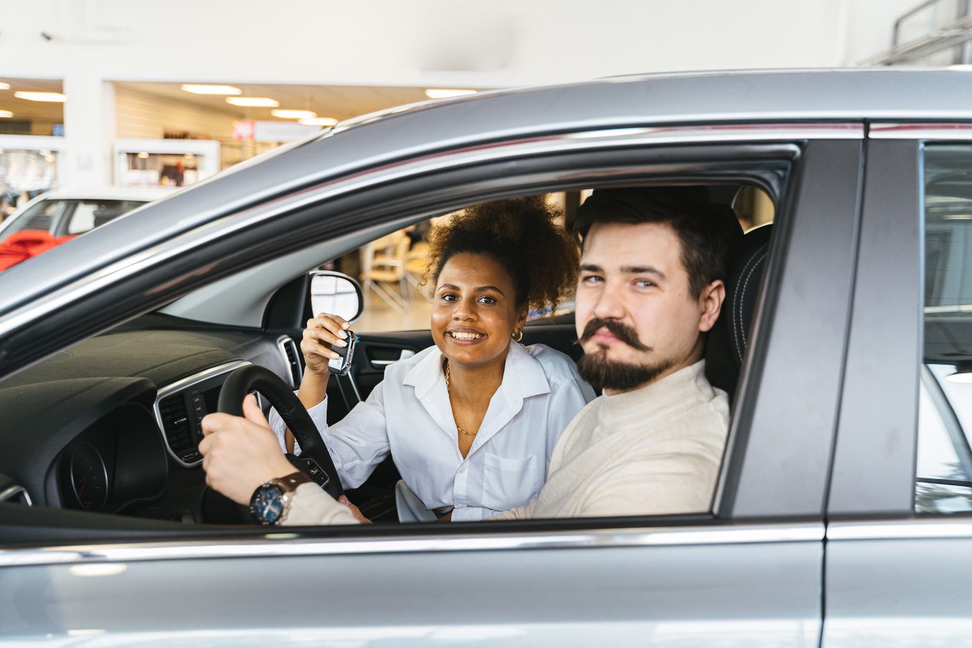 keychain for car keys — A smiling couple sitting inside a new car, holding the key and looking pleased