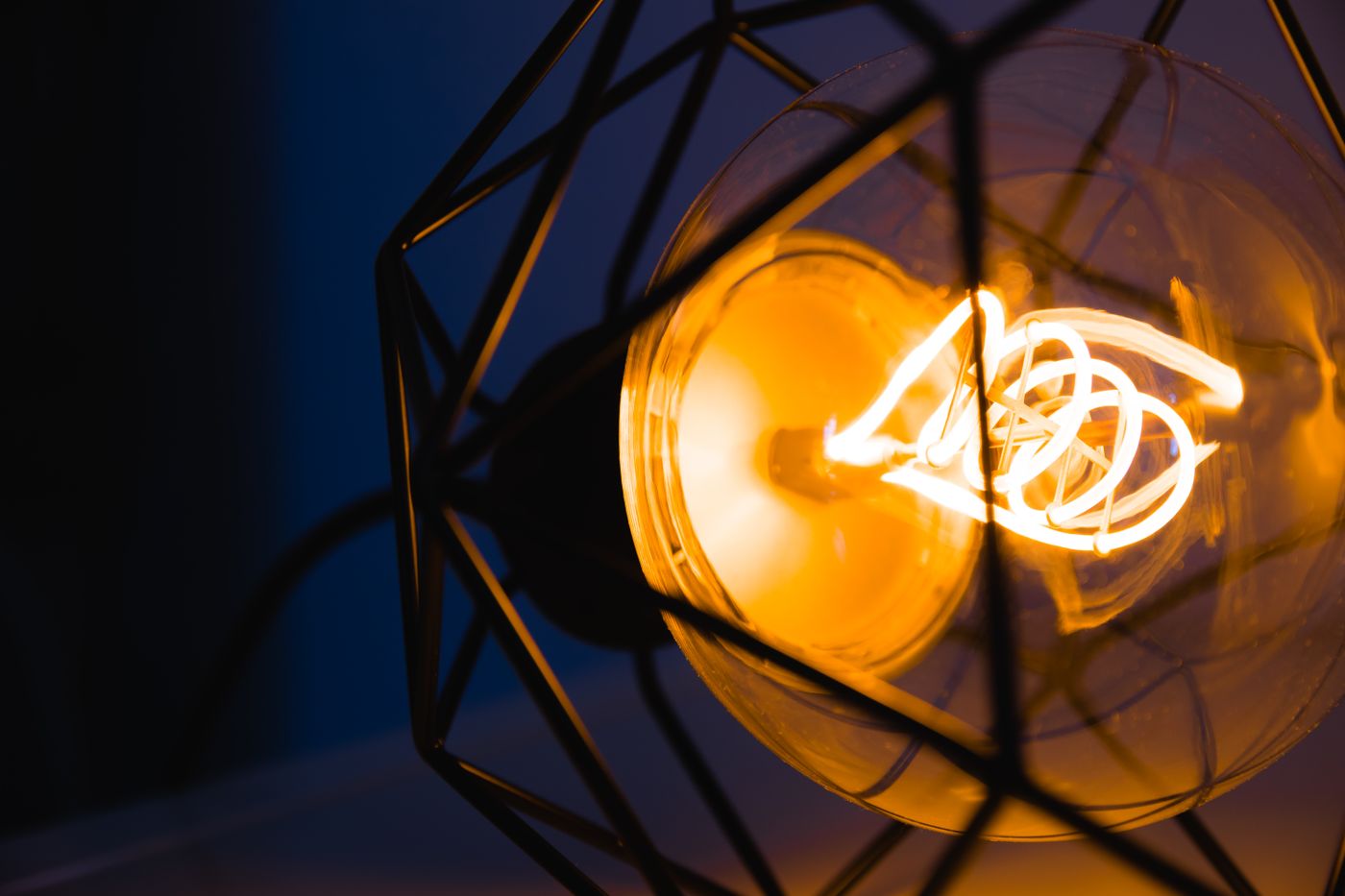 filament drying — A glowing light bulb captured in a metal geometric frame, illuminating its surroundings